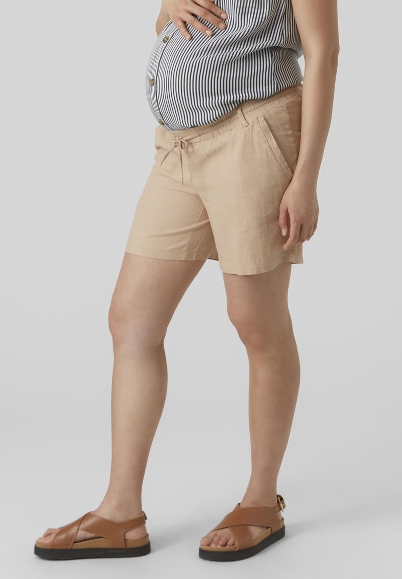 Shorts de un tono beige claro con un corte relajado, que cuentan con una cintura con cordón y bolsillos laterales. Combinados con sandalias marrones de tiras.