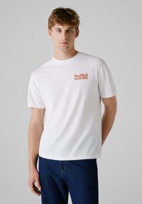 White cotton t-shirt featuring a red "Red Bull RACING" logo on the left chest, short sleeves, and a classic crew neck design.