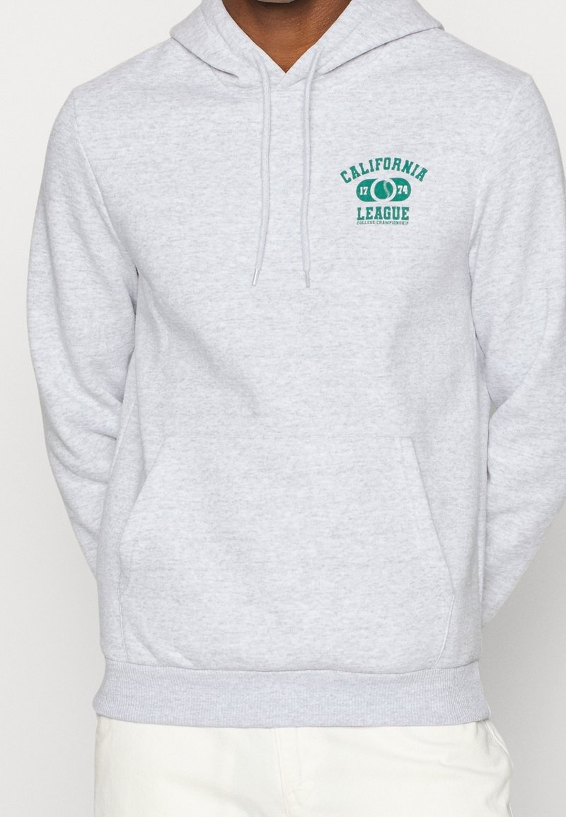 Persona che indossa una felpa grigia chiara con tasca frontale e testo verde "California League 1774 College Championship" sul lato sinistro del petto.