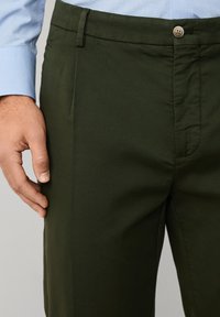 Pantaloni verde măsliniu dintr-un material neted, cu o curea în față, închidere cu nasture și croială dreaptă.