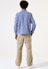 Blauw en wit geruit button-up shirt, beige broek, achteraanzicht. Katoenen stof, lange mouwen, zakken op de broek, en witte sneakers.