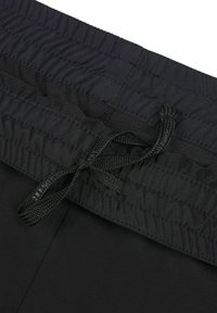 Nærbillede af sort elastisk linning med syede detaljer og bundet snor på sorte stofbukser.