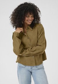 Olijfgroene button-up shirt in een gestructureerde stof, met een kraag en oversized mouwen, gecombineerd met lichtblauwe jeans.