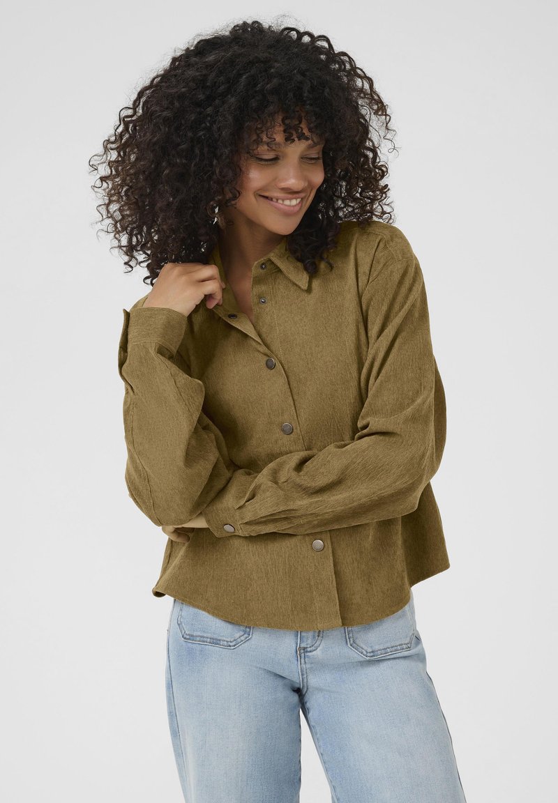 Olijfgroene button-up shirt in een gestructureerde stof, met een kraag en oversized mouwen, gecombineerd met lichtblauwe jeans.