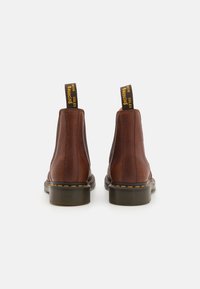 Braune Leder-Stiefeletten mit strukturiertem Finish, elastischen Seitenpaneelen und gelben Zuglaschen mit der Aufschrift "MIT SPRINGFÄHIGEN SOHLEN", runde Zehenform.