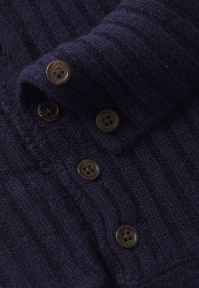 Cardigan de punto acanalado en color marino con cuello solapa y cinco botones marrones, que muestra una textura única y un detalle de cerca.