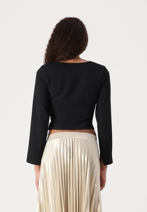 Black long-sleeve crop top with a round neckline, featuring a smooth texture. Paired with a pleated, shiny, knee-length skirt in light gold.