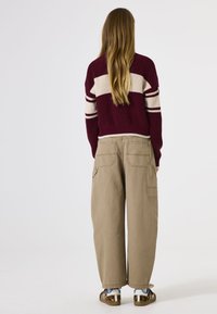 Burgunderfarbener Strickpullover mit weißen Streifen, kombiniert mit lockeren beigen Cargo-Hosen mit Taschen und einem umgeschlagenen Saum. Braune und weiße Schuhe.