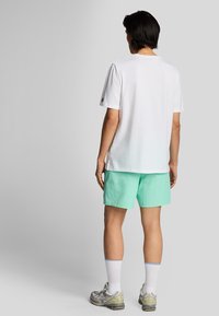 Maglietta bianca in cotone a maniche corte, abbinata a pantaloni corti verde menta con texture. Modello che indossa calze bianche e scarpe sportive grigie.