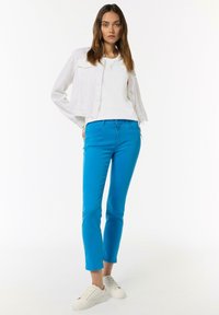 Niebieskie spodnie slim-fit w połączeniu z białą koszulką i jasnobeżową kurtką typu cropped, dopełnione białymi trampkami.