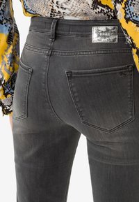 Jeans de mezclilla gris con una textura suave. Presentan dos bolsillos traseros y una etiqueta de marca plateada encima del bolsillo derecho.