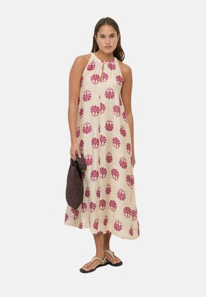 Mujer con vestido midi sin mangas beige con estampado floral rosa, llevando un bolso tejido oscuro y sandalias beige.