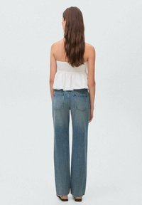 Lightweight white strapless top with a ruffled hem, paired with high-waisted, faded blue wide-leg jeans, showing a relaxed fit.