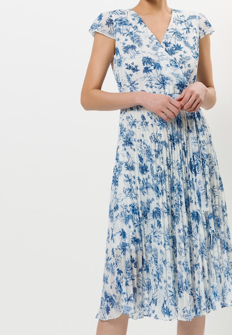 Robe portefeuille florale en blanc et bleu avec manches courtes, design plissé et décolleté en V présentant un motif botanique sur toute la surface.