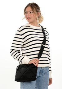Young woman wearing a white and black striped sweater and jeans, carrying a quilted black crossbody bag with a wide strap.