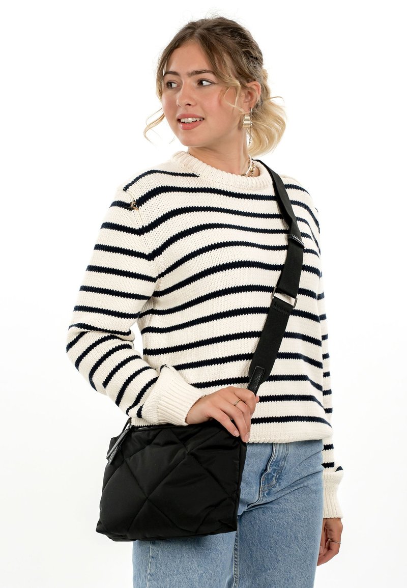 Young woman wearing a white and black striped sweater and jeans, carrying a quilted black crossbody bag with a wide strap.