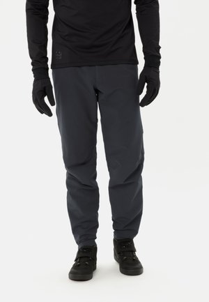 Pantalons d'extérieur gris foncé en matériau léger et résistant à l'eau. Présentent une coupe décontractée et sont associés à des gants et des chaussures noirs.