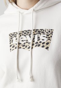 Bílá mikina s kapucí a šňůrkami, se vzorem velkého béžového a černého leopardího potisku loga Levi's. Měkká textilie.