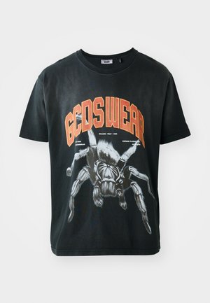 T-shirt en coton noir avec un grand graphique de araignée et le texte en orange "GCDSWEAR" en gras. Design à manches courtes et col rond.