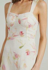 Blumenkleid aus leichtem Stoff mit sanften rosa Tulpenmustern. Geformtes Oberteil mit breiten Trägern und taillierter Passform.