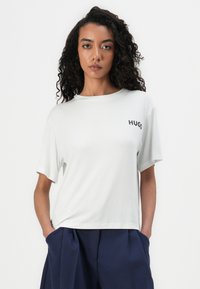 Vit bomulls t-shirt med korta ärmar, rund halsringning, lös passform, med "HUGO"-logotyp i svart på bröstet. Matcher med mörkblå byxor.
