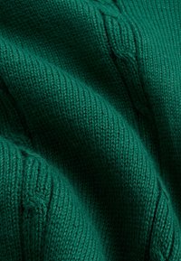 Tela de punto verde con patrones de trenzas, mostrando una textura detallada y tejido en capas suaves y plegadas.