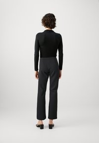 Top a maniche lunghe nera abbinato a pantaloni scuri aderenti. L'outfit presenta una silhouette slim e sandali neri con tacco basso.