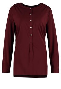 Bordårröd blus med lång ärm, rund halsringning, knappstängning och plisserad detalj fram. Mjukt tyg med en slät yta.