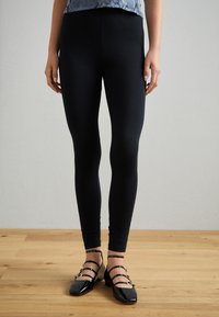 Leggings negros hechos de una tela elástica, que presentan una textura mate y suave, con un diseño ajustado que llega hasta los tobillos.