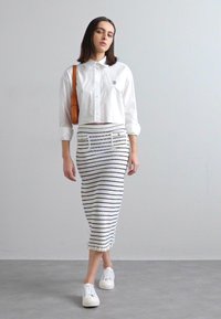 Cropped white shirt with button closure, paired with a form-fitting striped skirt in white and navy, and white sneakers. Includes a brown bag.