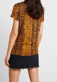 Krótki rękaw w kolorze pomarańczowym z czarnym nadrukiem węża; ma dopasowany krój i gładką fakturę. Zestawiony z dżinsową mini spódnicą z postrzępionym brzegiem.