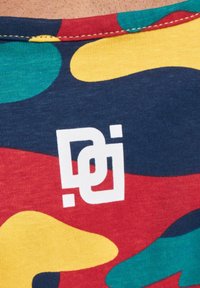 Țesătură colorată cu modele, prezentând forme mari de verde, galben, roșu și albastru închis. Un logo alb este vizibil în colțul din jos.