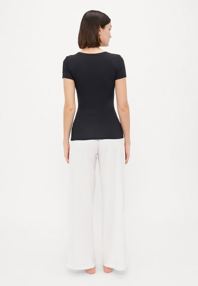 Black fitted t-shirt with short sleeves, crew neck, and smooth fabric. Paired with loose-fitting white trousers. Back view shown.