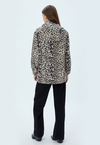 Jakke med leopardprint og hætte, lavet af letvægtsstof. Har lange ærmer, en løs pasform og er parret med sorte flared bukser.