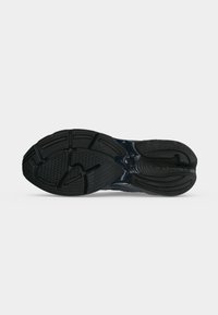 Semelle de basket noire avec motifs texturés sur la bande de roulement et logo « new balance » sur le talon, sur un fond clair uni.