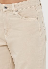 Beiga denimbyxor med en klassisk femficksdesign, metallknapp och synlig sömtextur.