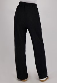 Zwarte textuurpant met een relaxte pasvorm, elastische tailleband en rechte benen. Bevat subtiele oppervlakte-details en een minimalistisch ontwerp.