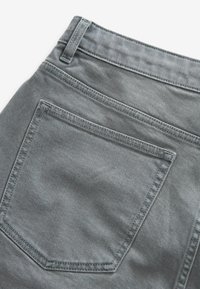 Jeans in denim grigio con una tasca posteriore singola decorata con un design ottagonale cucito e una texture visibile dal tessuto.
