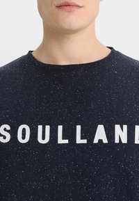 Felpa navy con texture a granuli, caratterizzata da grandi lettere bianche che scrivono "SOULLAND" sul petto, colletto rotondo e vestibilità comoda.