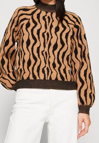 Brun- och svart randig tröja med ribbad halsringning och mudd, med ett vågformat mönster, tillverkad av mjukt stickat tyg.