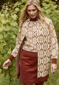 Pull et cardigan en mélange de laine couleur crème avec des motifs géométriques rouille, associés à une jupe en velours côtelé rouille. Texture douce et design ajusté.