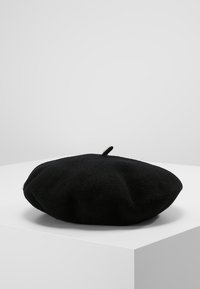 Béret preto de lã, com uma forma arredondada e um pequeno laço superior, apresentando uma superfície suave e texturada, com um design minimalista.