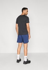 Svart kortermet skjorte kombinert med bl�å treningsshorts, svarte joggesko og hvite ankelsokker, sett bakfra.