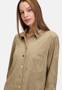 Khaki zamszowa koszula zapinana na guziki z kołnierzykiem, długimi rękawami, kieszonką z przodu i guzikami w srebrnym kolorze; miękka tekstura i minimalistyczny design.
