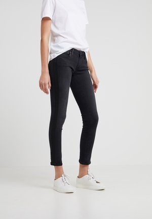 Jeans negros ajustados con un corte slim, diseño de cinco bolsillos y un ligero estiramiento. Llevados con una camiseta blanca y zapatillas blancas.