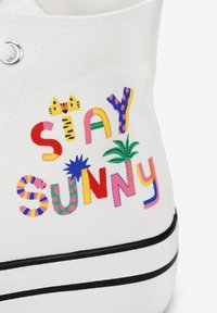 Sneaker bianco in tela con lettere ricamate multicolori e giocose che formano la scritta "STAY SUNNY", con suola in gomma nera e dettagli a motivi.