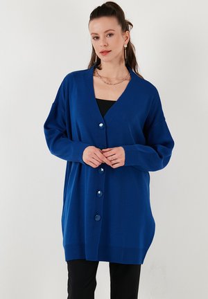 Cardigan à boutons en bleu vif, fabriqué en tissu doux, avec un col en V, une coupe décontractée, et de grands boutons bleus sur le devant.