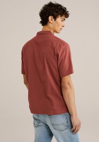 Korte mouw shirt in baksteenrood met een gestructureerd ruitpatroon, voorzien van een klassieke kraag en een rechte zoom, gecombineerd met lichtblauwe jeans.