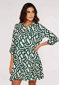 Grünes und cremefarbenes gemustertes Hemdblusenkleid mit gestuften Saum, langen Ärmeln und entspannter Passform. V-Ausschnitt und Taschendetails sind ebenfalls enthalten.