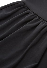 Zwarte stof met een zachte, matte textuur, met geplooide rimpels langs de tailleband, wat zorgt voor een soepel vallende drape.